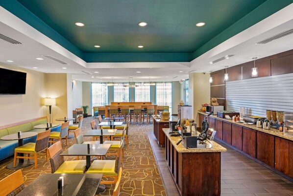 Comedor de hotel con diversas opciones de asientos, incluyendo boxes y mesas, y una zona de bar central con mostrador y varios servicios.
