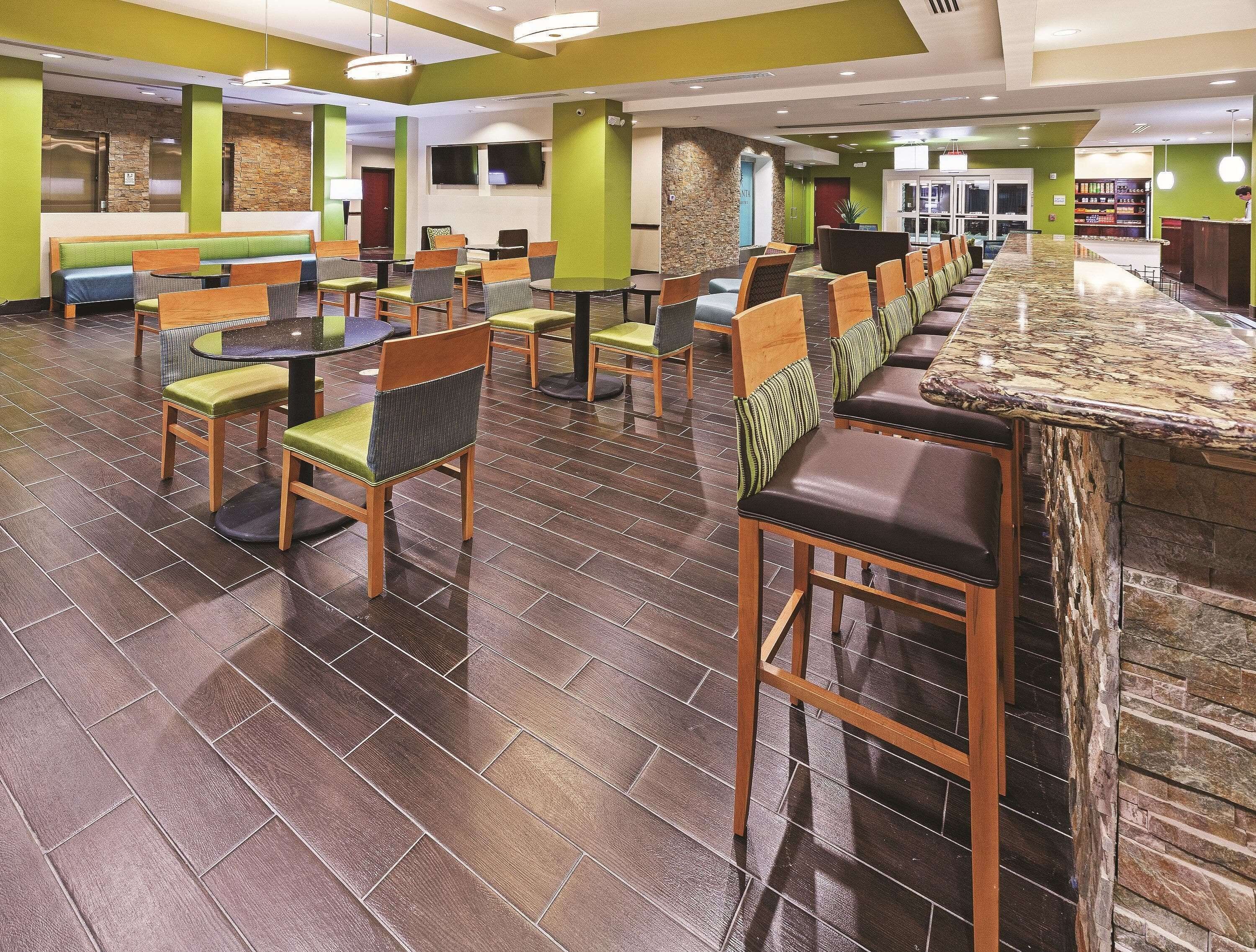 A hotel lobby with a long reception counter, multiple seating areas with chairs and sofas, and a stone accent wall.