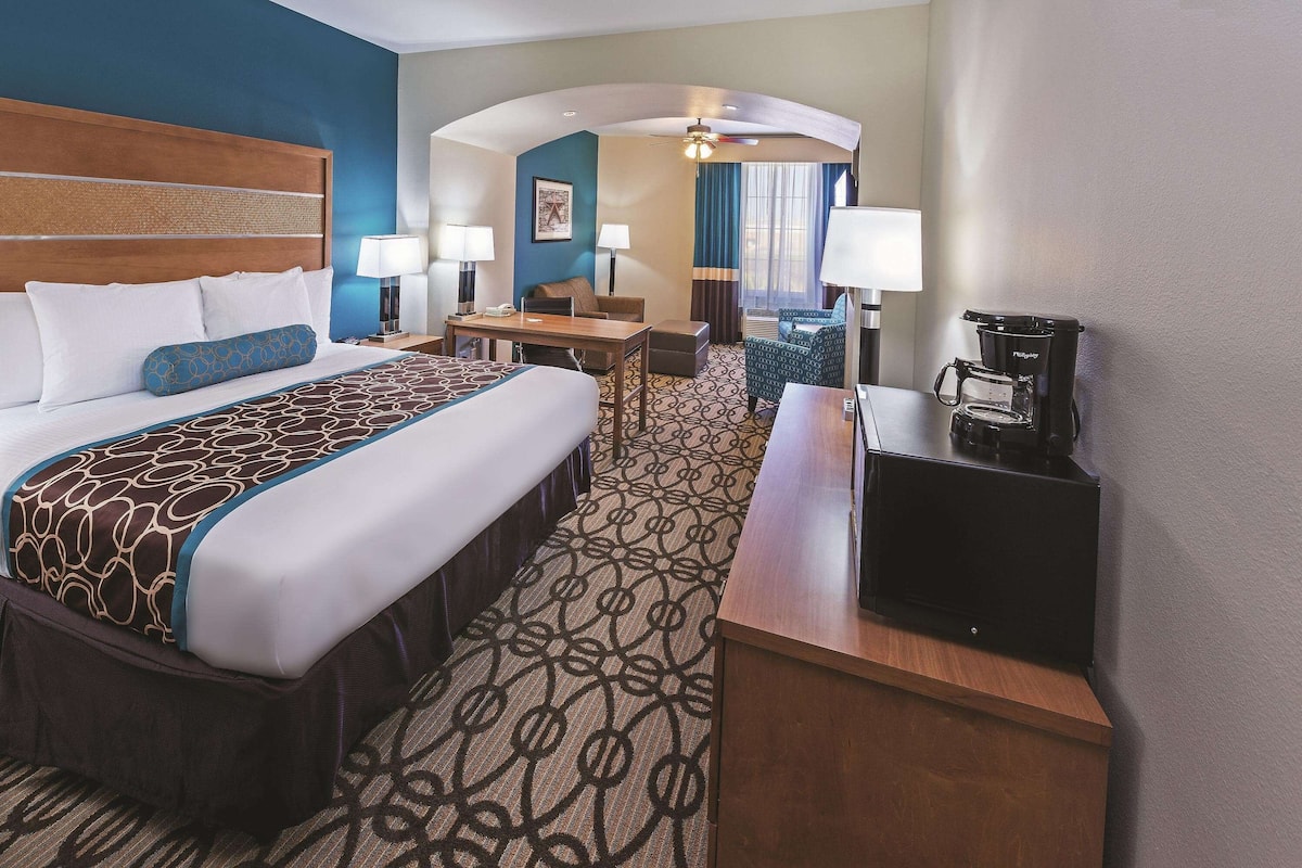 A hotel room with a large bed, a desk, a coffee maker, and a seating area with a chair and table.
