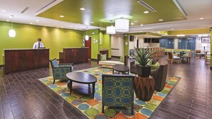 A hotel lobby with a reception desk, seating area, and a large plant. - La Quinta by Wyndham Houston Willowbrook Vintage Park (Houston)