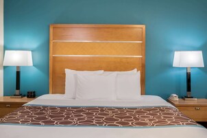 Habitación de hotel con cabecera de madera, ropa de cama blanca y manta decorativa estampada. Hay dos mesitas de noche con lámparas y un teléfono en cada una.