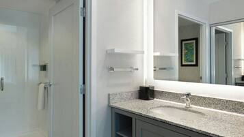 Une salle de bain moderne avec une porte de douche en verre, un grand miroir et un comptoir en granit.