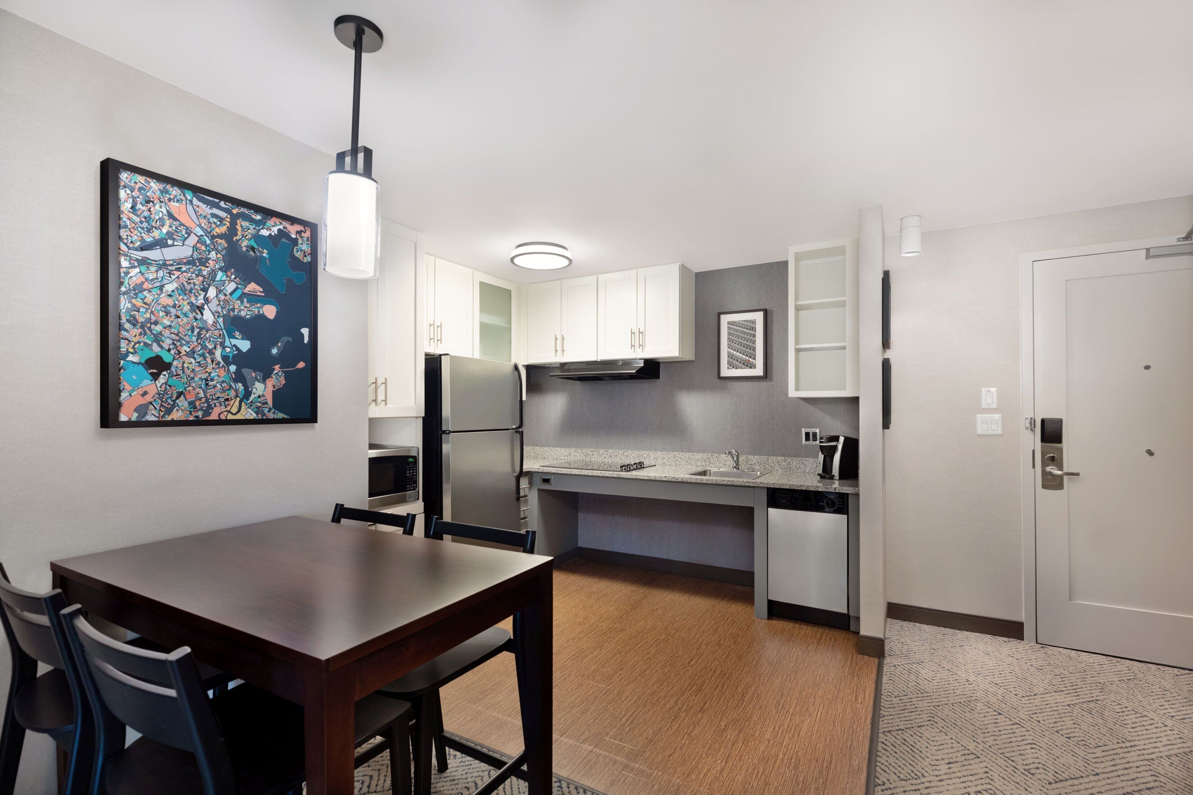 A modern kitchen with white cabinets, a built-in oven, and a dining area with a table and chairs.