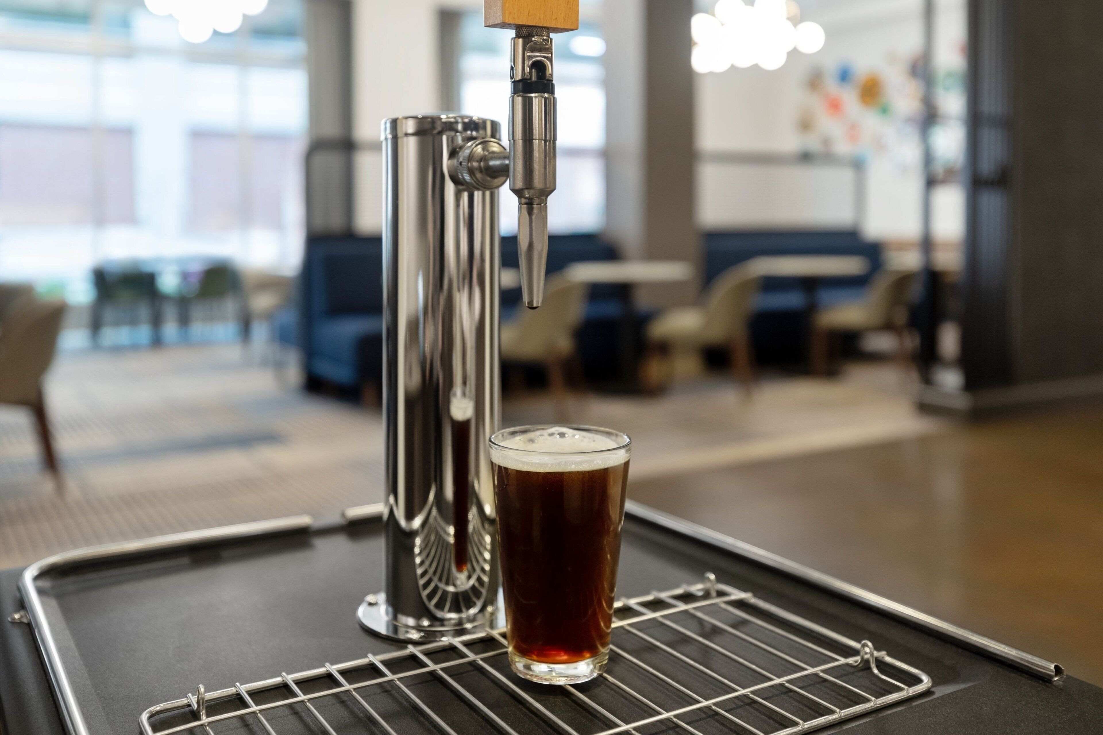 A tap dispensing beer into a glass on a wire rack in a modern indoor setting.