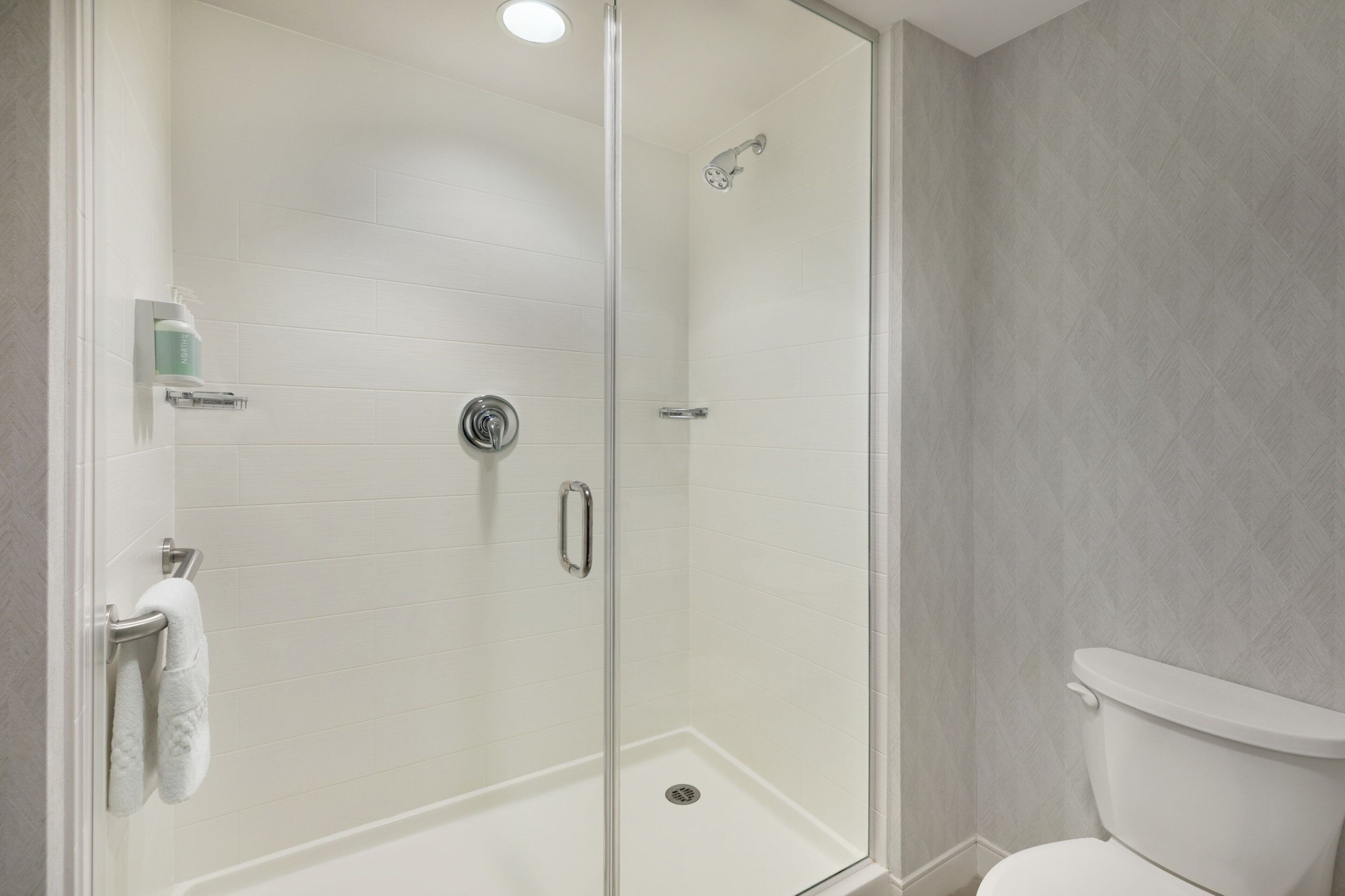 A modern bathroom with a glass-enclosed shower, a toilet, and a towel rack.