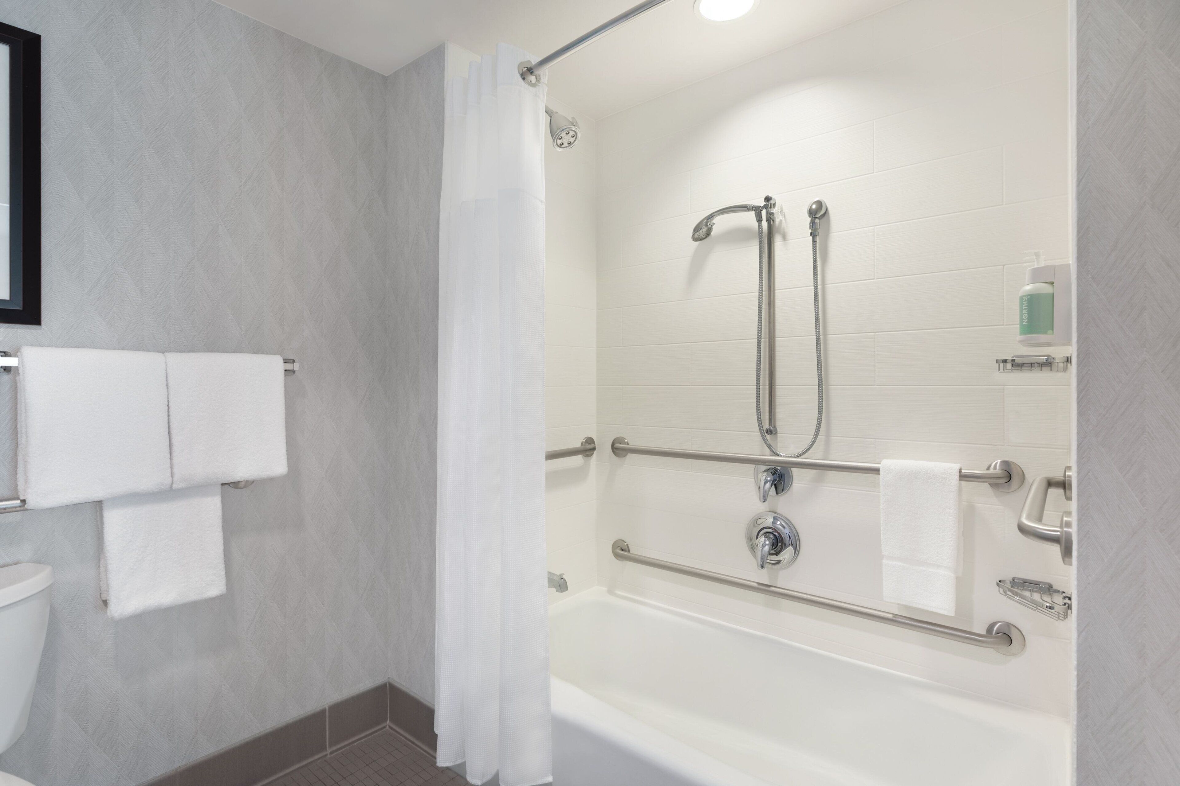 A modern bathroom with a shower, grab bars, and a toilet.