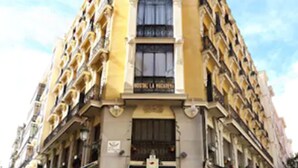 Un edificio en esquina con fachada amarilla, varios balcones y mesas al aire libre.