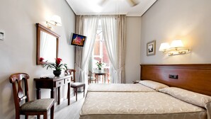 Una habitación de hotel con dos camas, un escritorio con silla, televisión y ventana con cortinas.