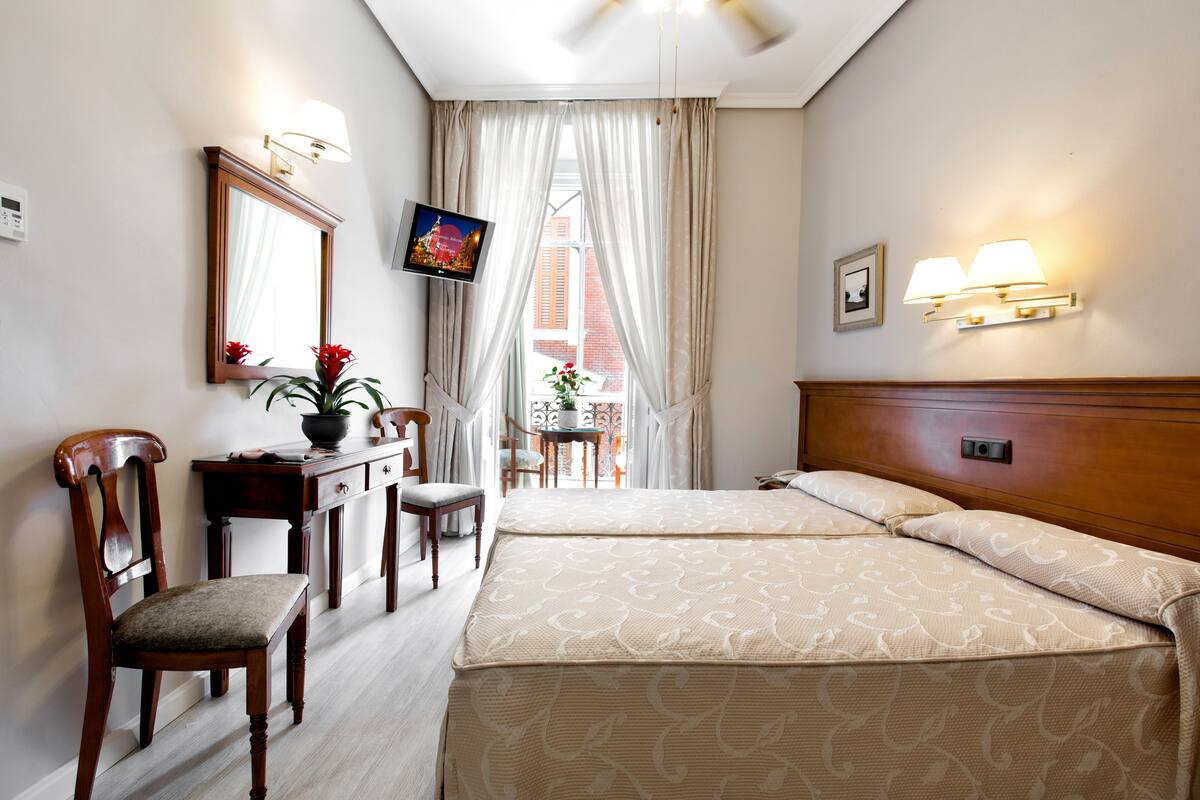 A hotel room with two beds, a desk with a chair, a television, and a window with curtains.