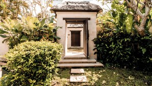 Un sentier mène à une petite construction fermée, dotée d’un toit de chaume et entourée d’une végétation luxuriante.