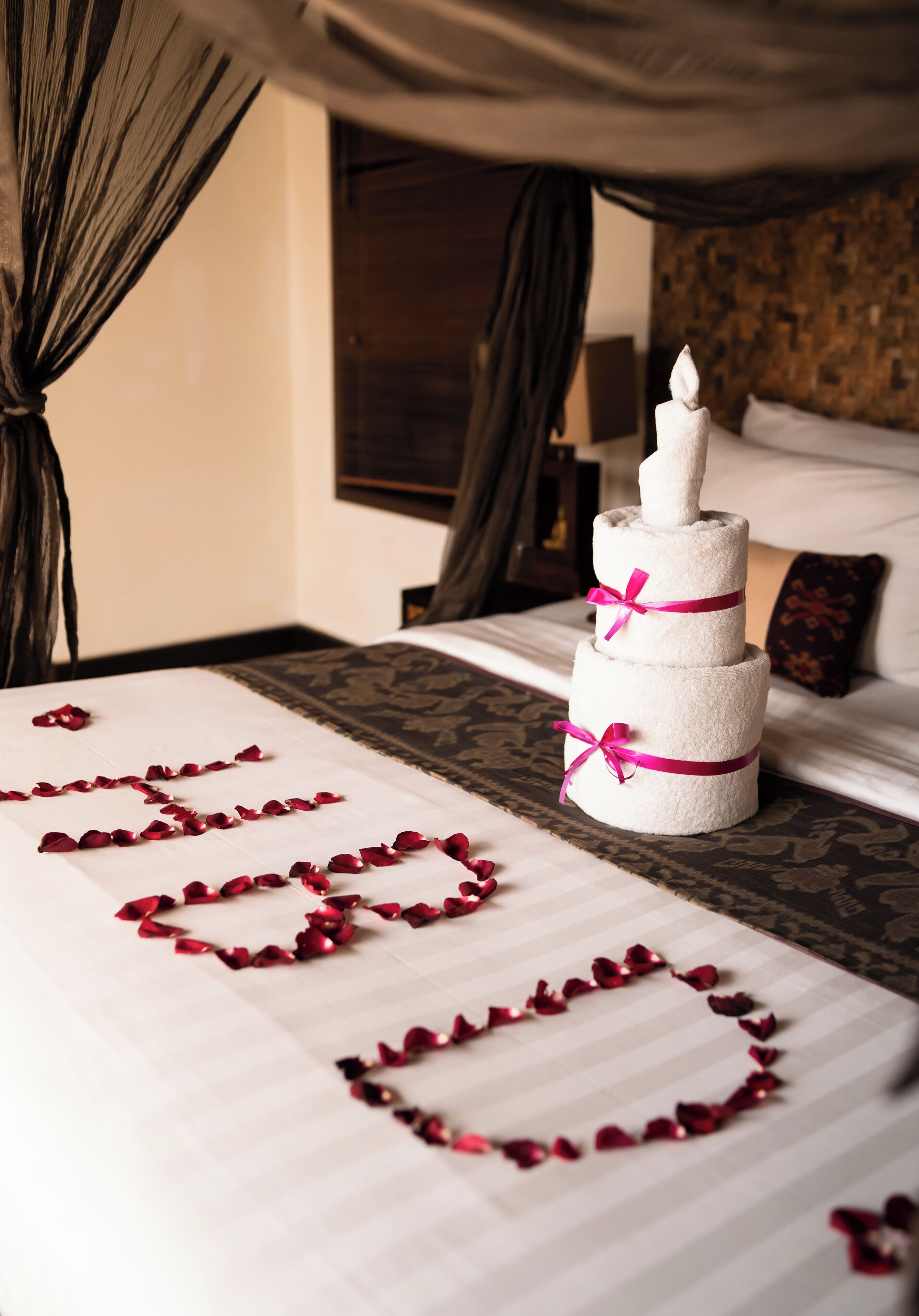 Una cama con pétalos de rosa dispuestos en forma de corazón y una vela sobre una mesita de noche.