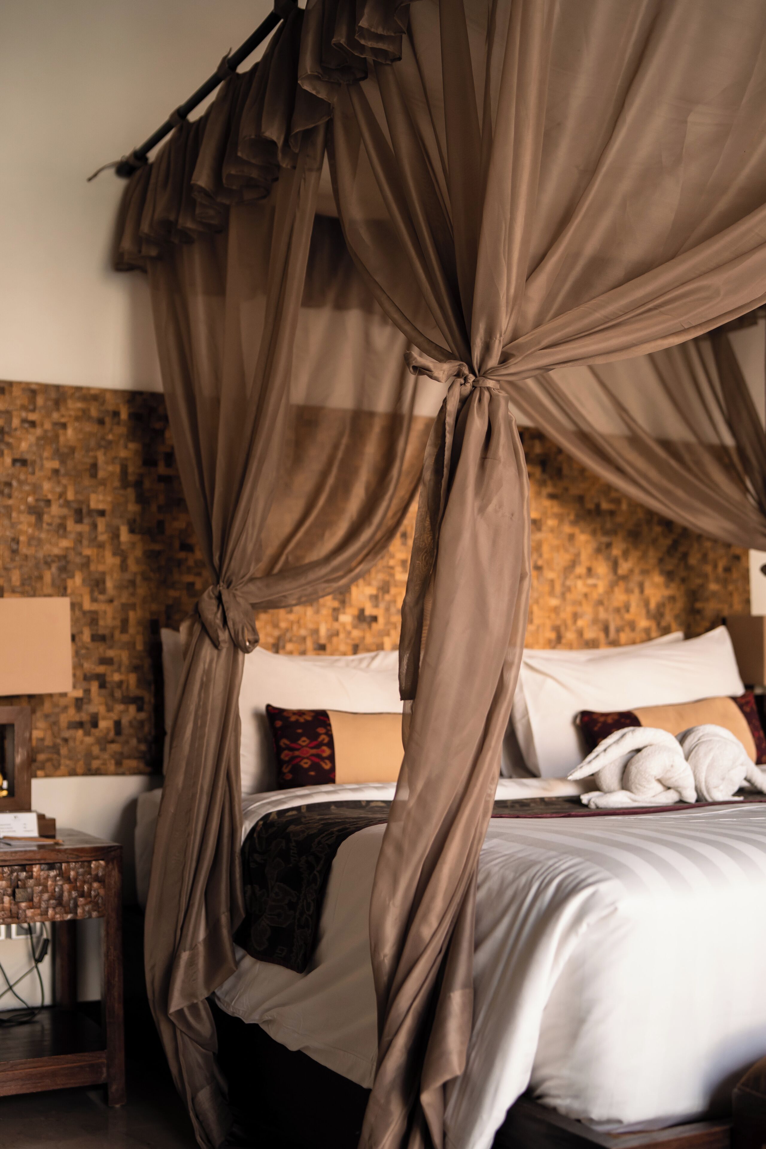 A bedroom with a canopy bed, a wooden nightstand, and a textured wall.