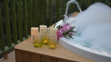 A wooden bench with candles and a bouquet of flowers beside a hot tub.