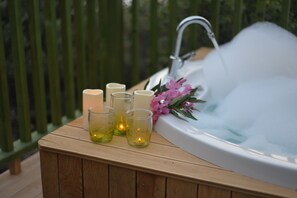 A wooden bench with candles and a bouquet of flowers beside a hot tub.
