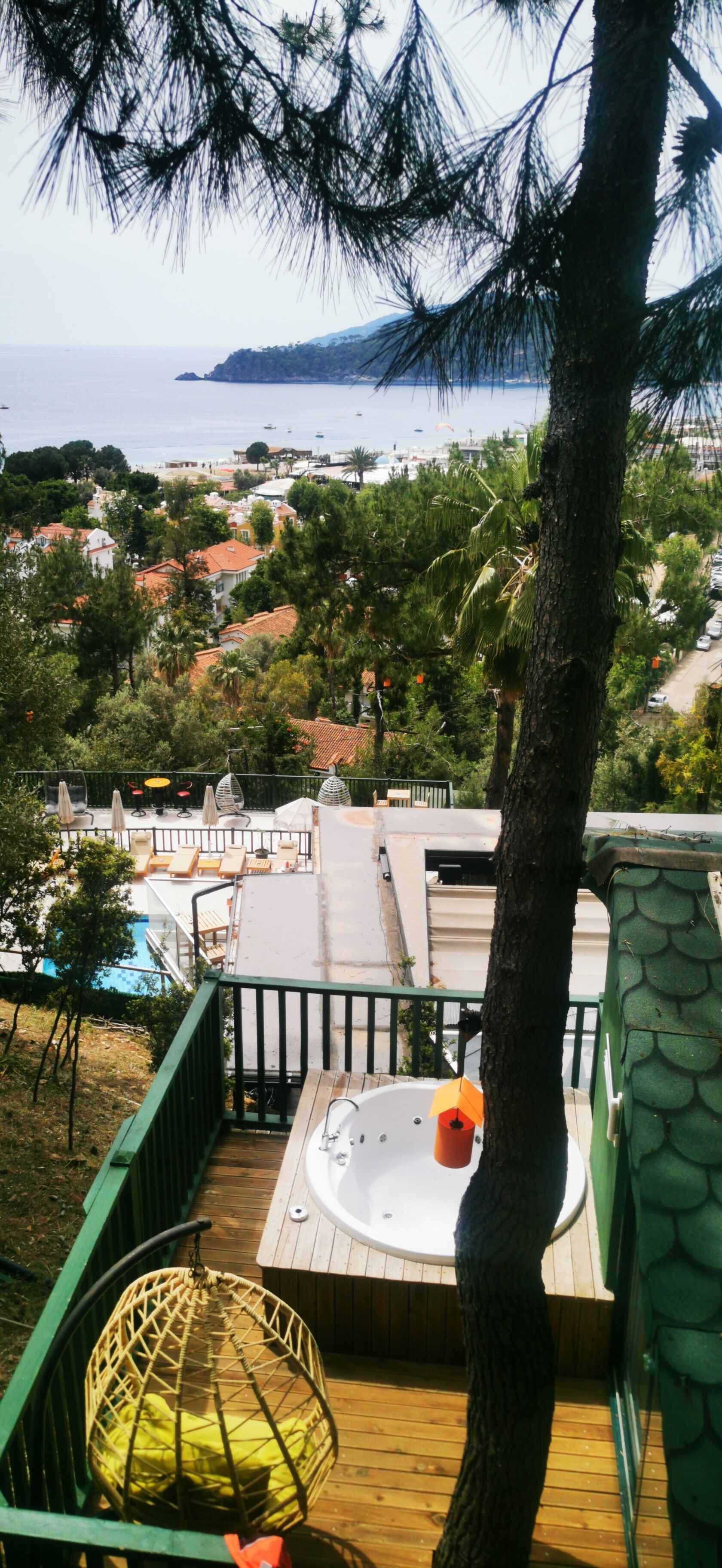 A deck with a hot tub, lounge chairs, and a view of the sea and buildings.