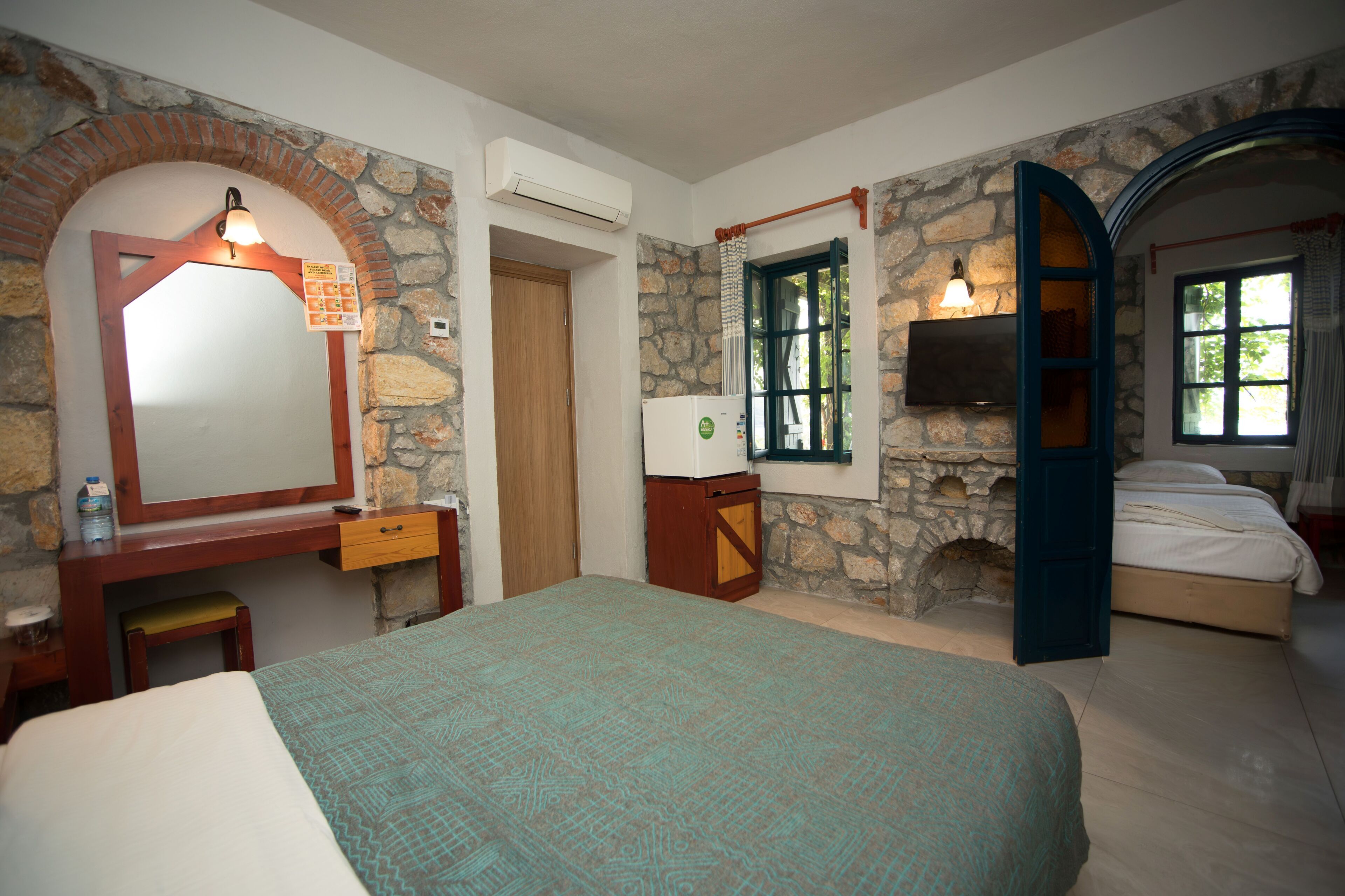 A bedroom with a bed, a dresser, a mirror, a stone wall, and a window.