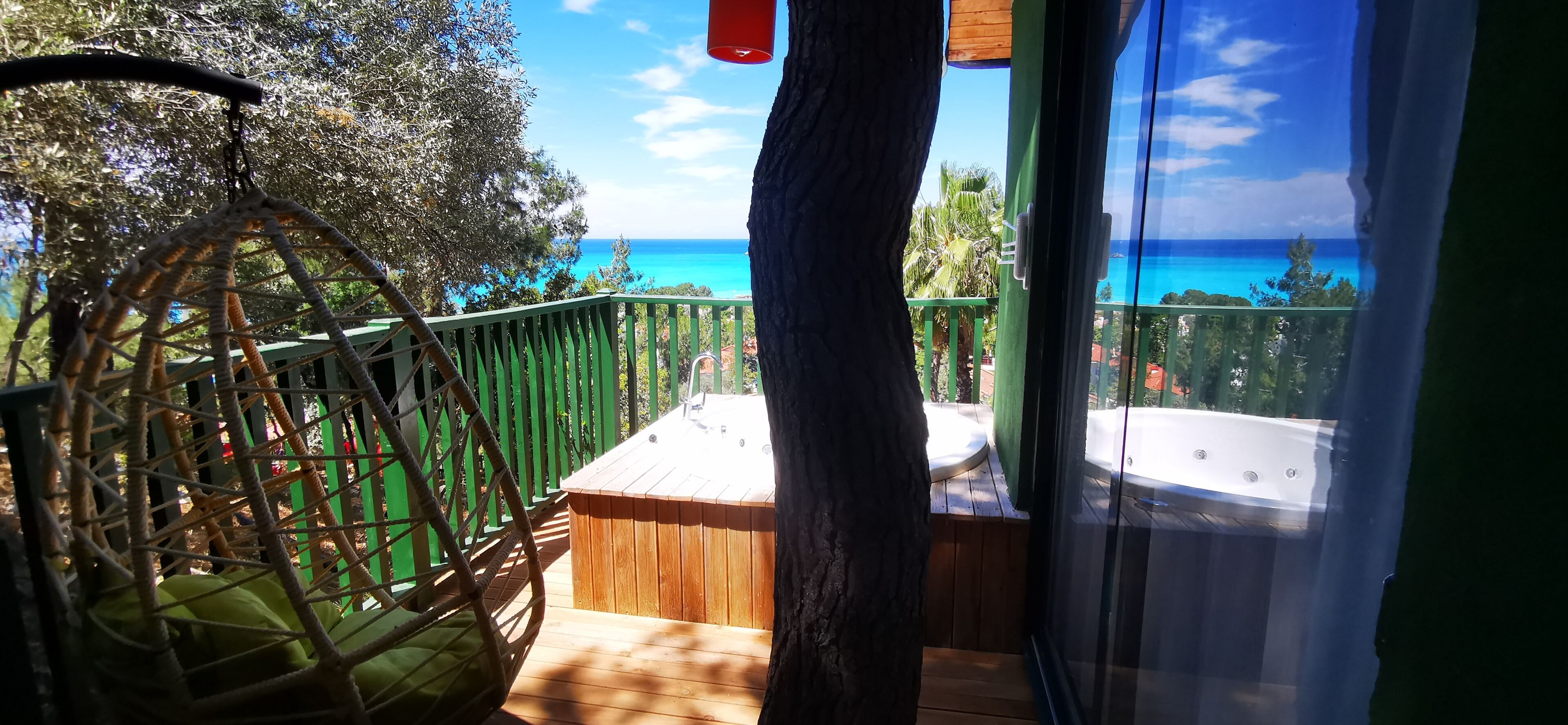 A balcony with a wicker chair, a wooden deck, and a hot tub.