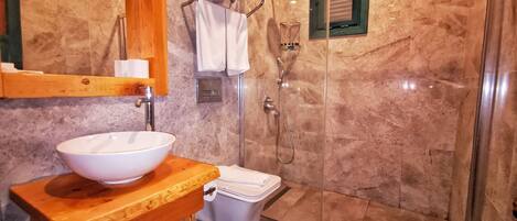 Une salle de bain avec un lavabo blanc, un meuble-vasque en bois, une douche à parois de verre et un mur recouvert de carreaux de marbre.