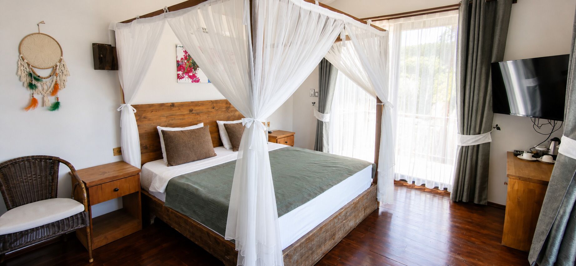 A bedroom with a four-poster bed, a bedside table, a chair, a television, and a dreamcatcher on the wall.