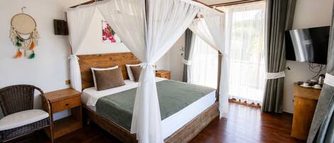 A bedroom with a four-poster bed, a bedside table, a chair, a television, and a dreamcatcher on the wall.