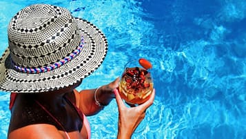 A person in a pool with a checkered hat and a drink.