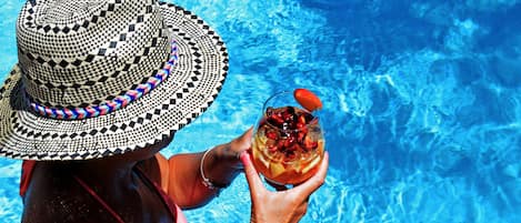 A person in a pool with a checkered hat and a drink.
