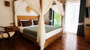 Une chambre à coucher avec un lit à baldaquin, une table de chevet en bois, un fauteuil en osier et un téléviseur fixé au mur.