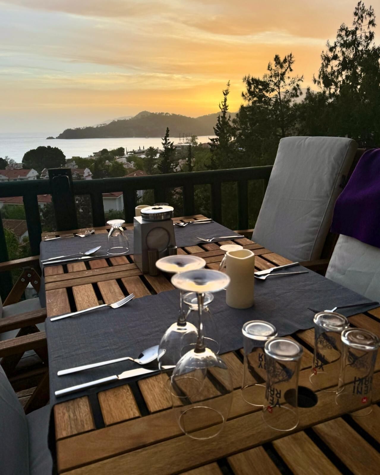 A wooden deck with a table set for a meal, overlooking a scenic view of a body of water and distant land.