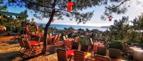 Outdoor seating with tables and chairs, a heart-shaped decoration, and a view of the sea.