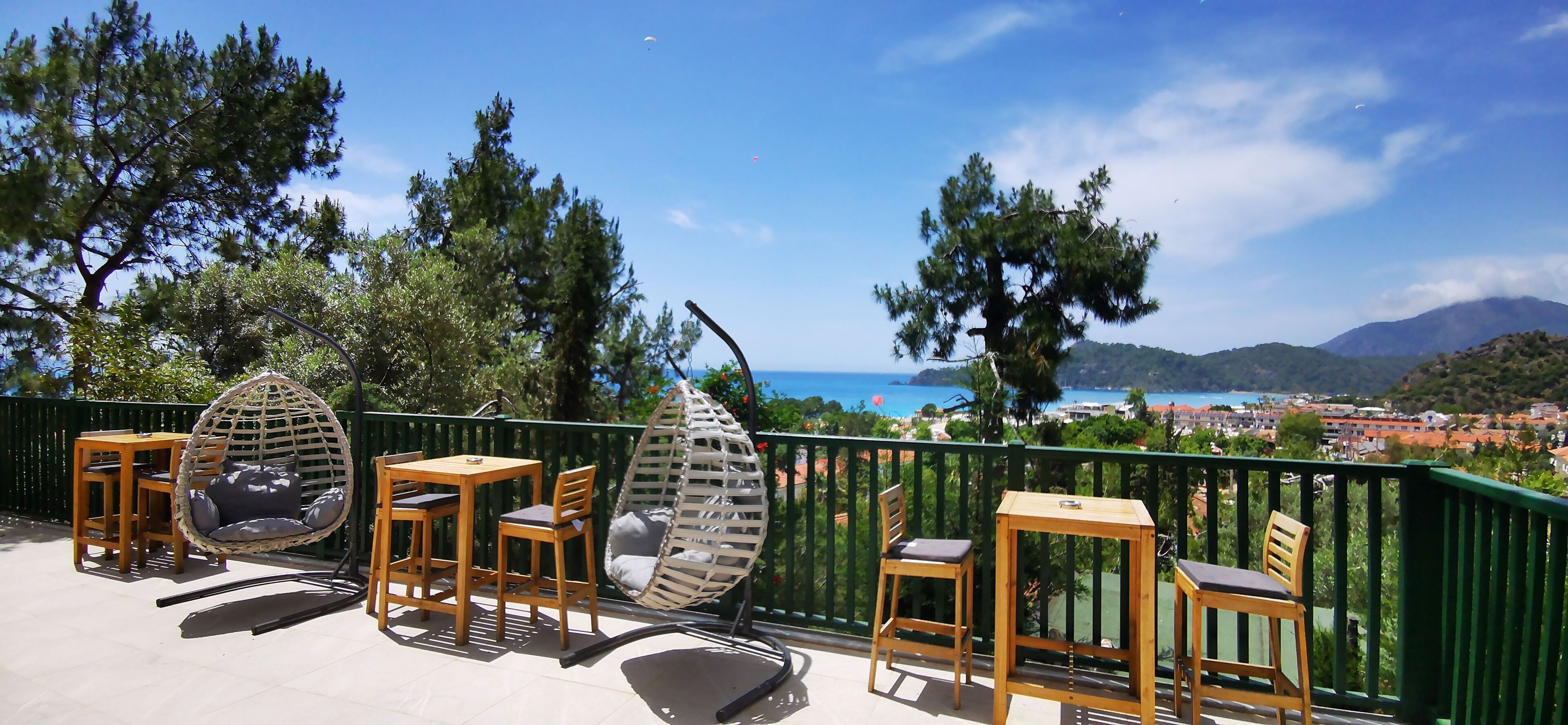 Une terrasse dotée de mobilier d’extérieur, offrant une vue sur la mer et agrémentée d’une rambarde verte.
