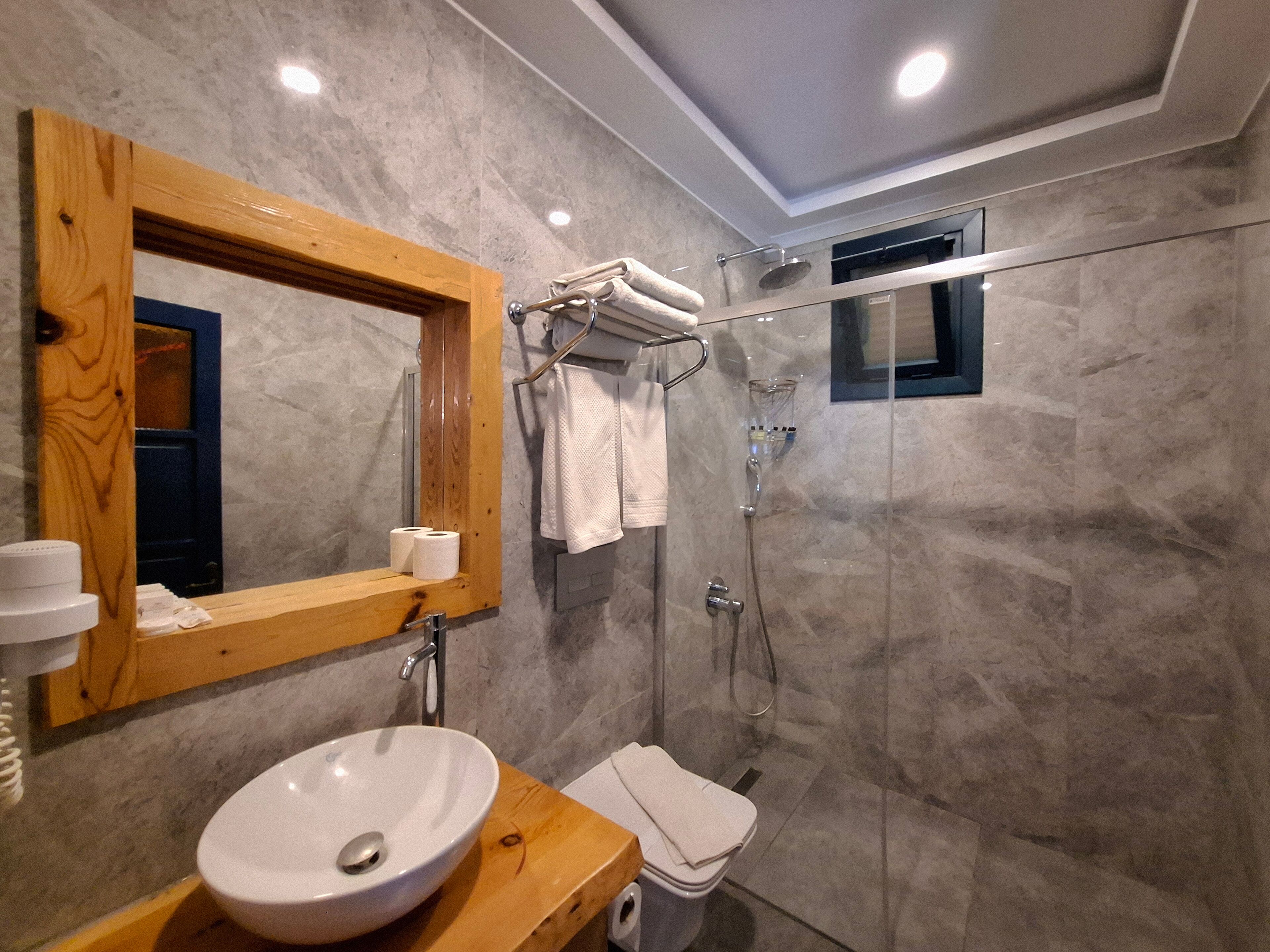 A modern bathroom with a wooden vanity, a large mirror, a white sink, a glass shower enclosure, and a towel rack.