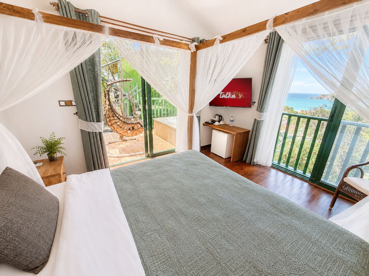A bedroom with a bed, a desk, a chair, and a view of the sea.