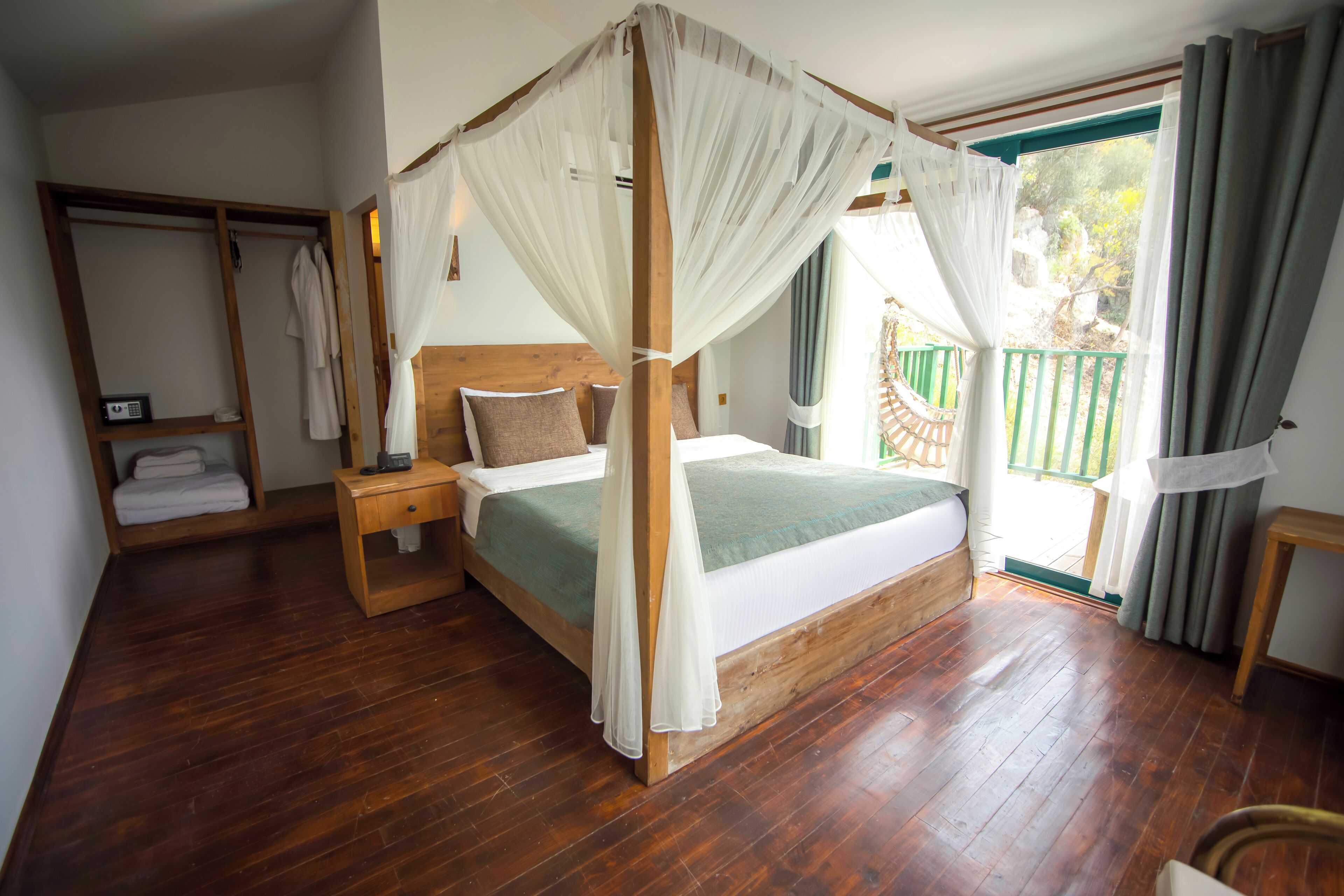 A bedroom with a four-poster bed, wooden headboard, and a view of a green outdoor area.
