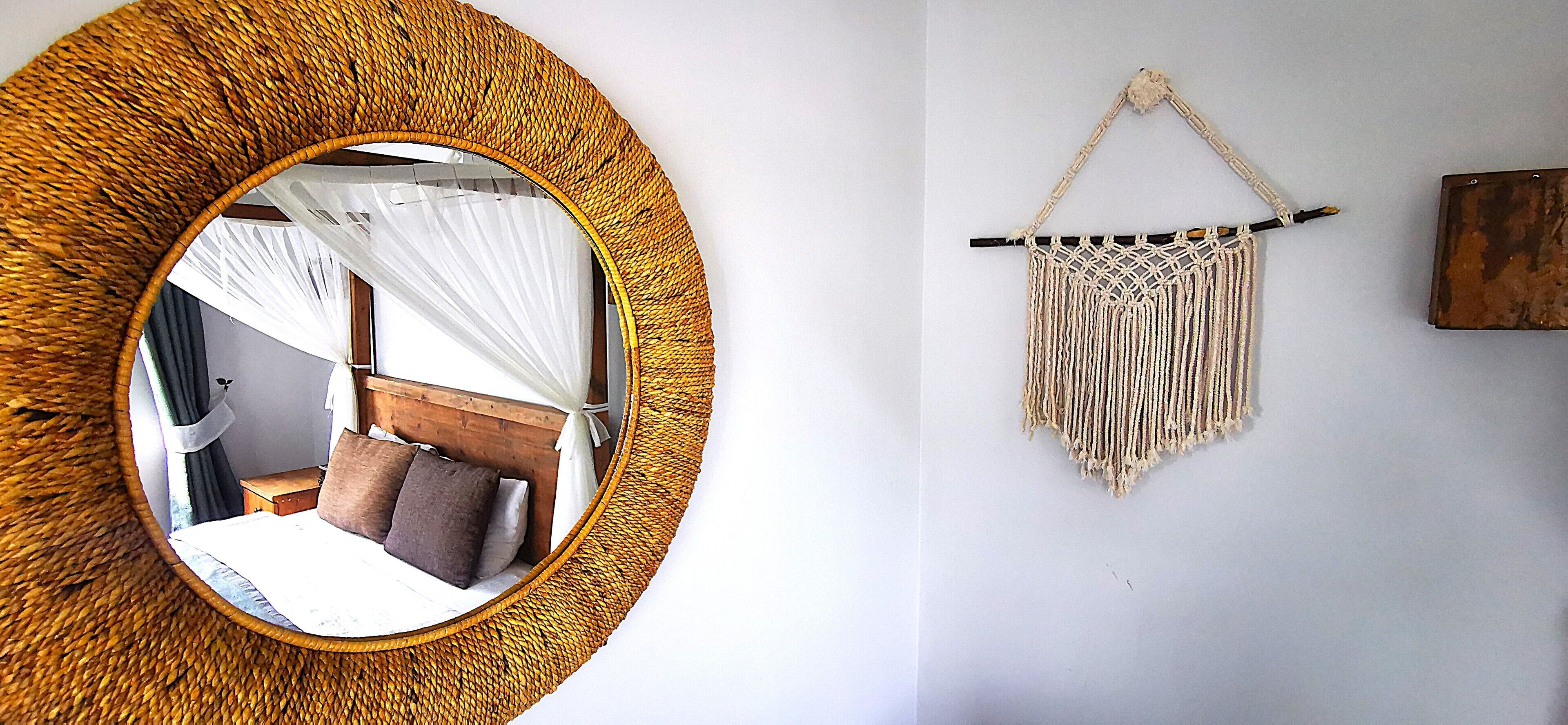 A room with a round mirror, a macrame wall hanging, and a bed with a wooden headboard.