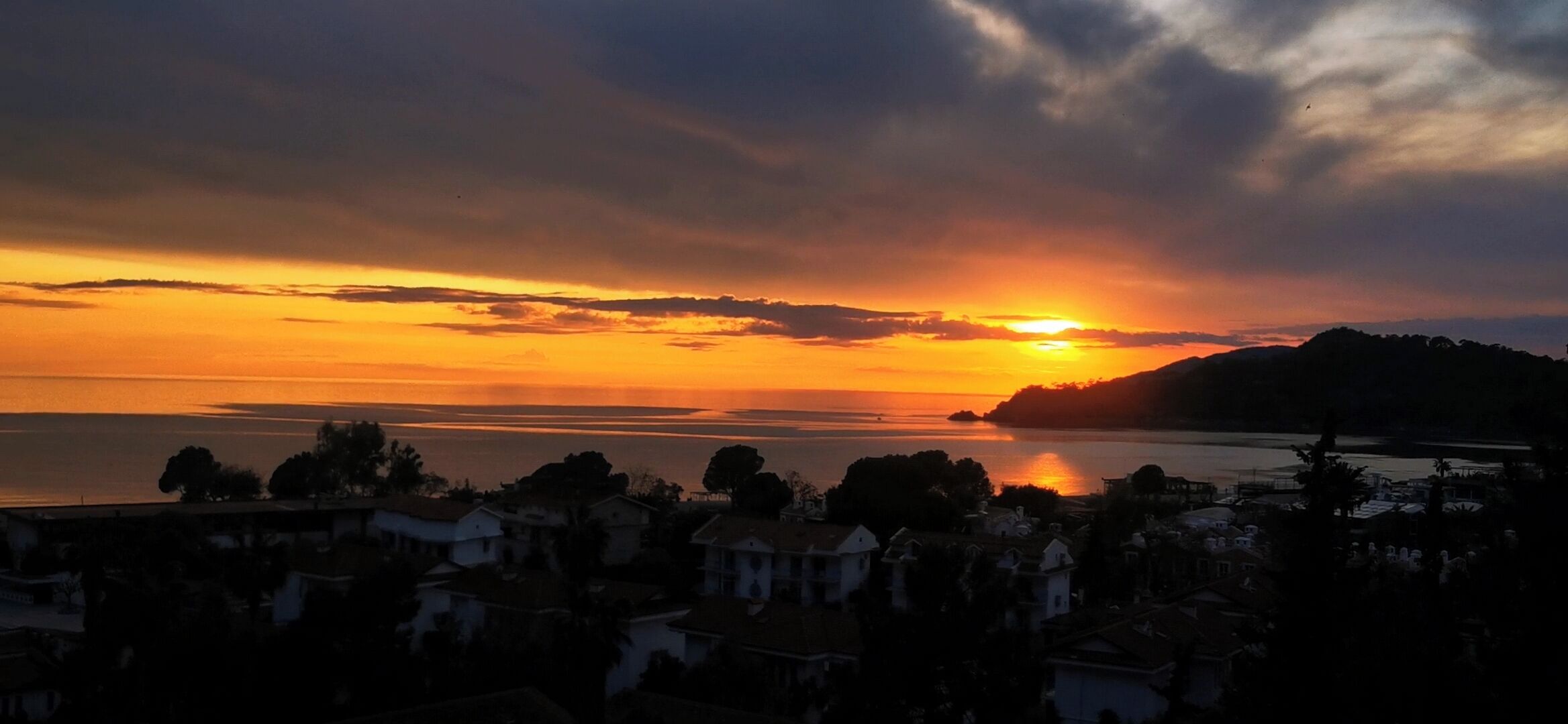 A coastal sunset view with houses in the foreground.