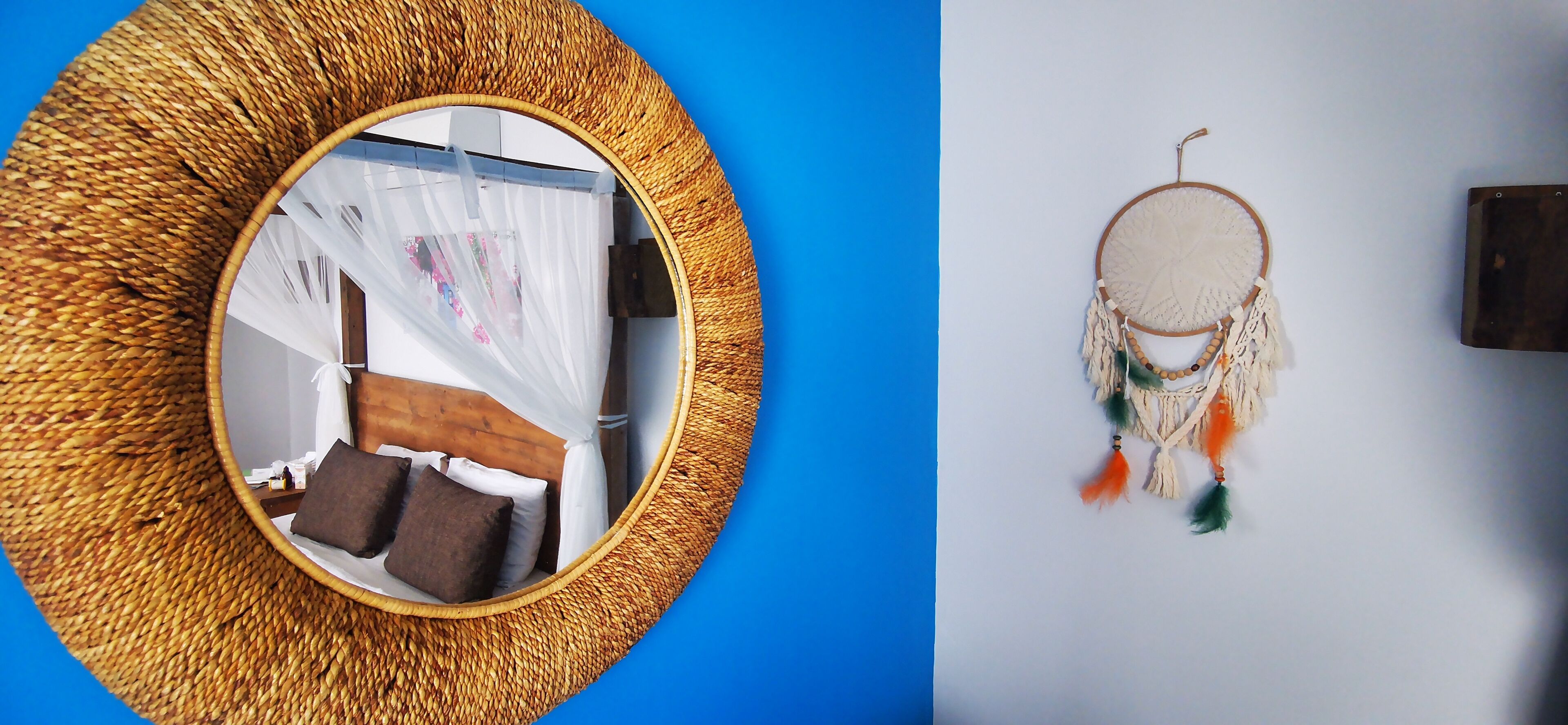 A room with a woven round mirror, a bed with brown and white bedding, and a dreamcatcher on the wall.