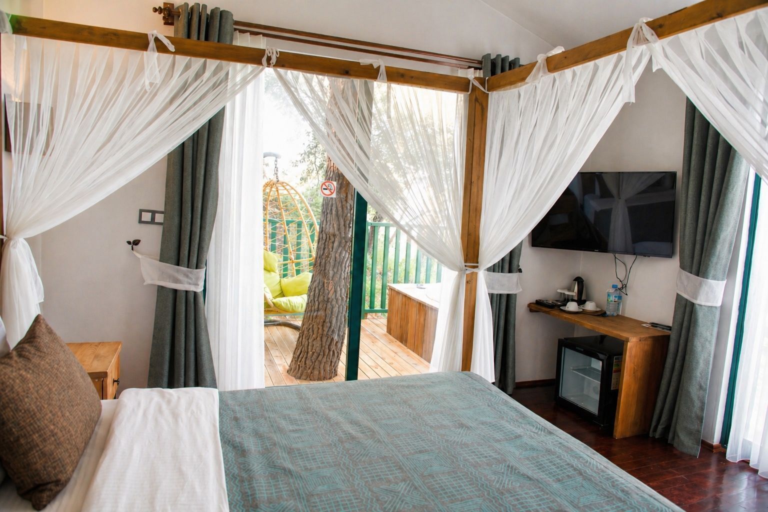 A bedroom with a bed, a desk, a TV, and a view of an outdoor area.