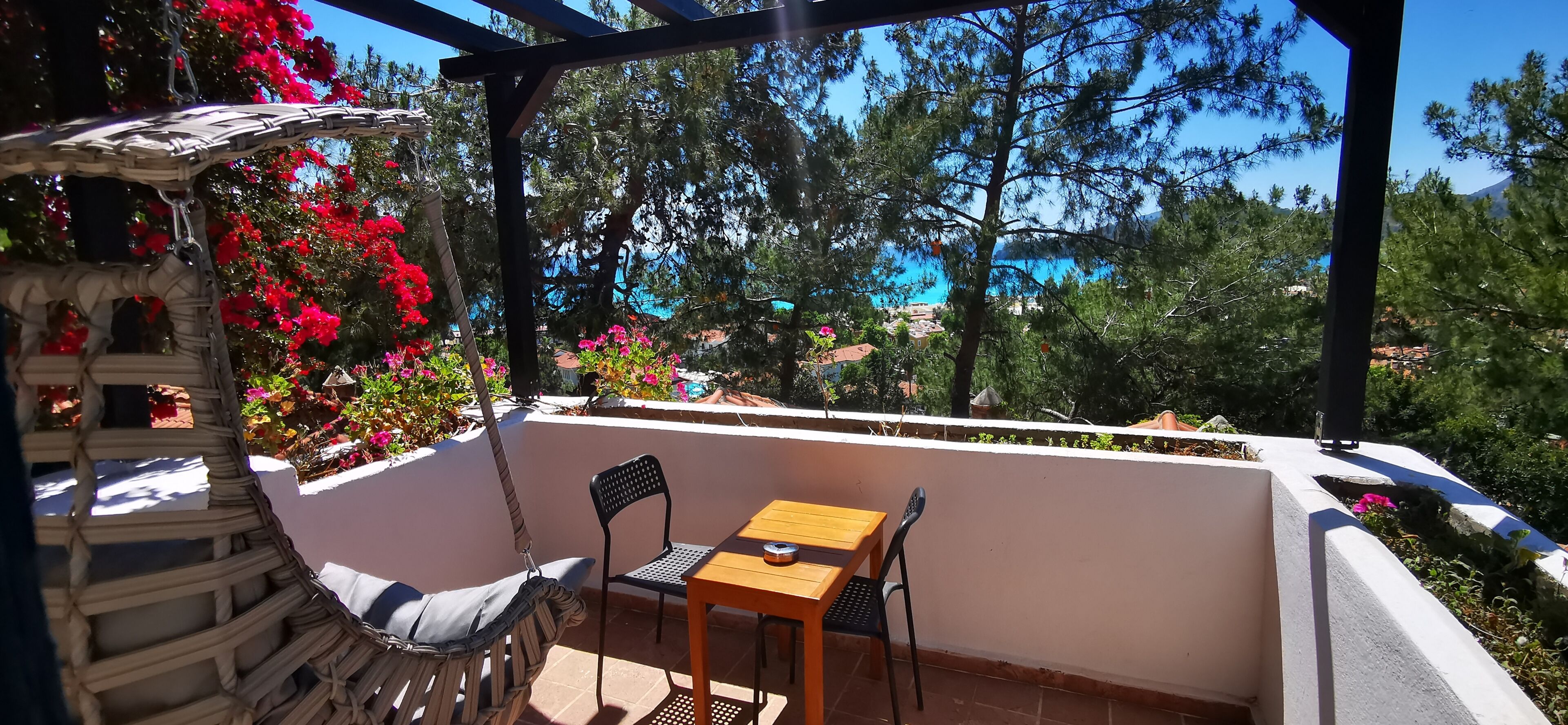 A balcony with a wooden table and chairs, surrounded by potted plants and flowers.