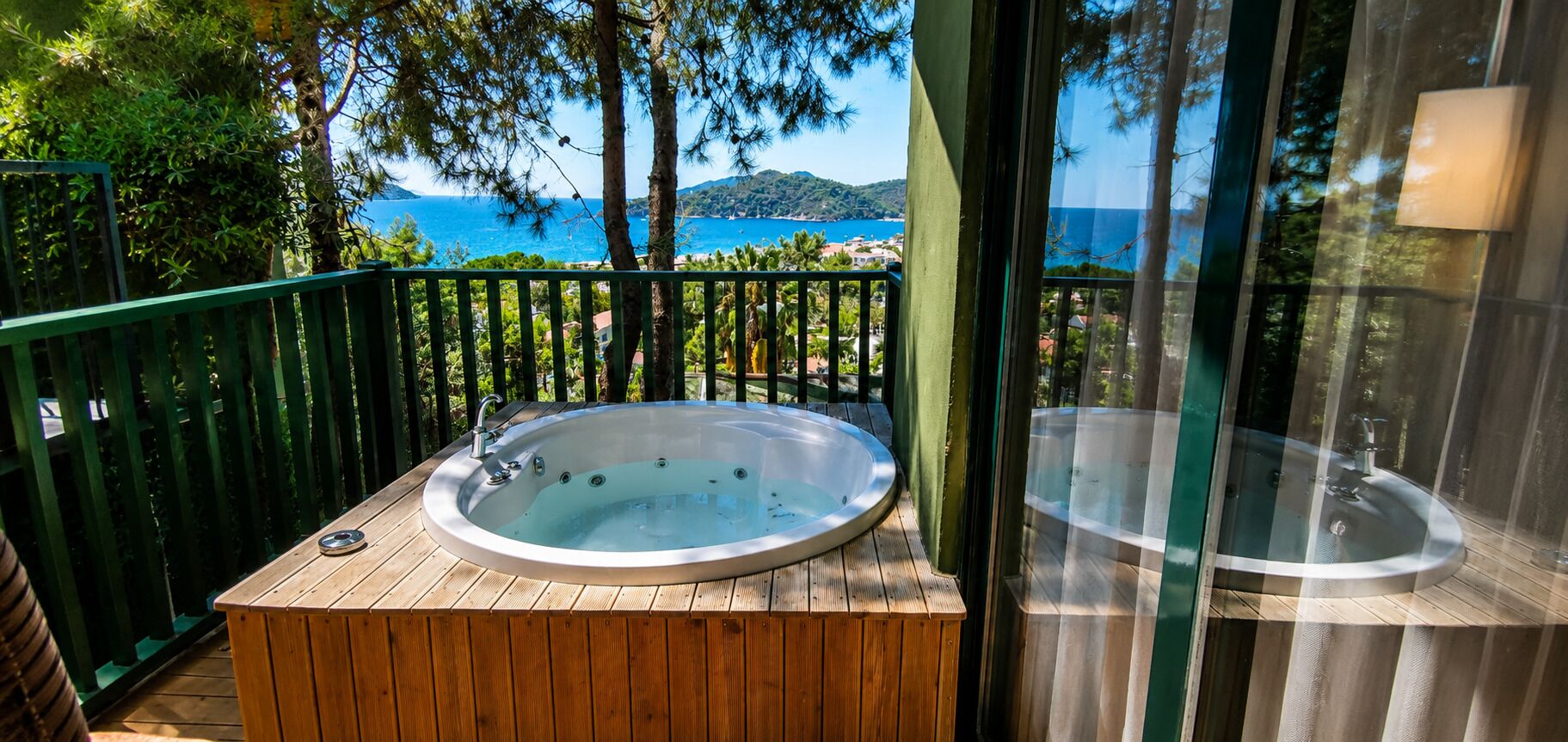 Una terraza de madera con un jacuzzi y un lavamanos, con vistas panorámicas del mar y las colinas.