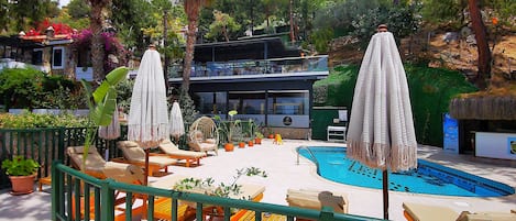 Zona junto a la piscina con sillones de descanso, sombrillas y una piscina.