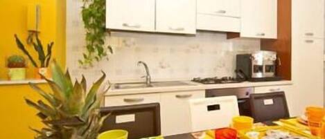 A kitchen with white cabinets, a sink, and a stove. There is a table with food and a pineapple.