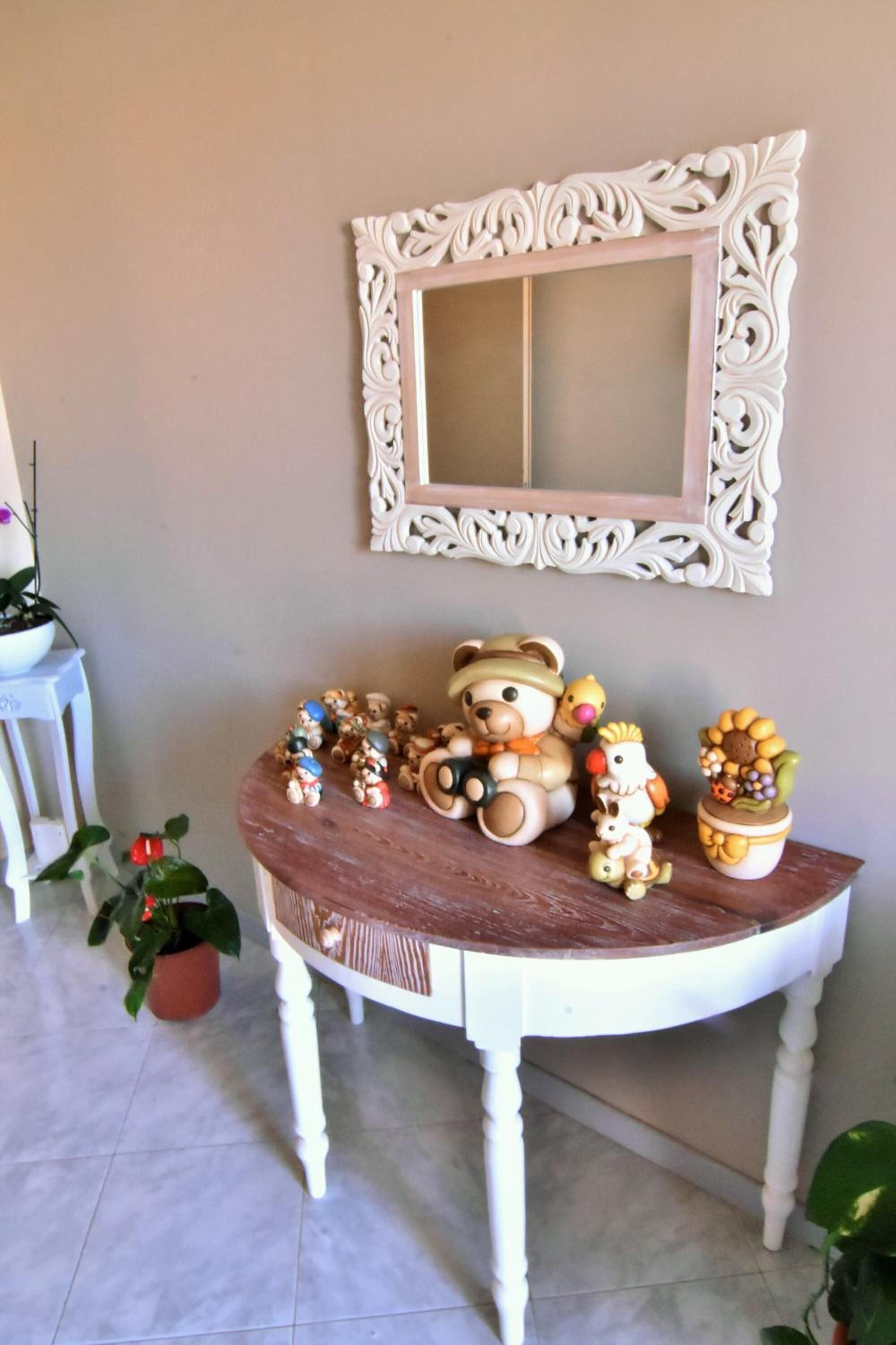 Un tavolo in legno bianco con uno specchio sopra, circondato da vari oggetti decorativi tra cui figurine e un piccolo vaso.