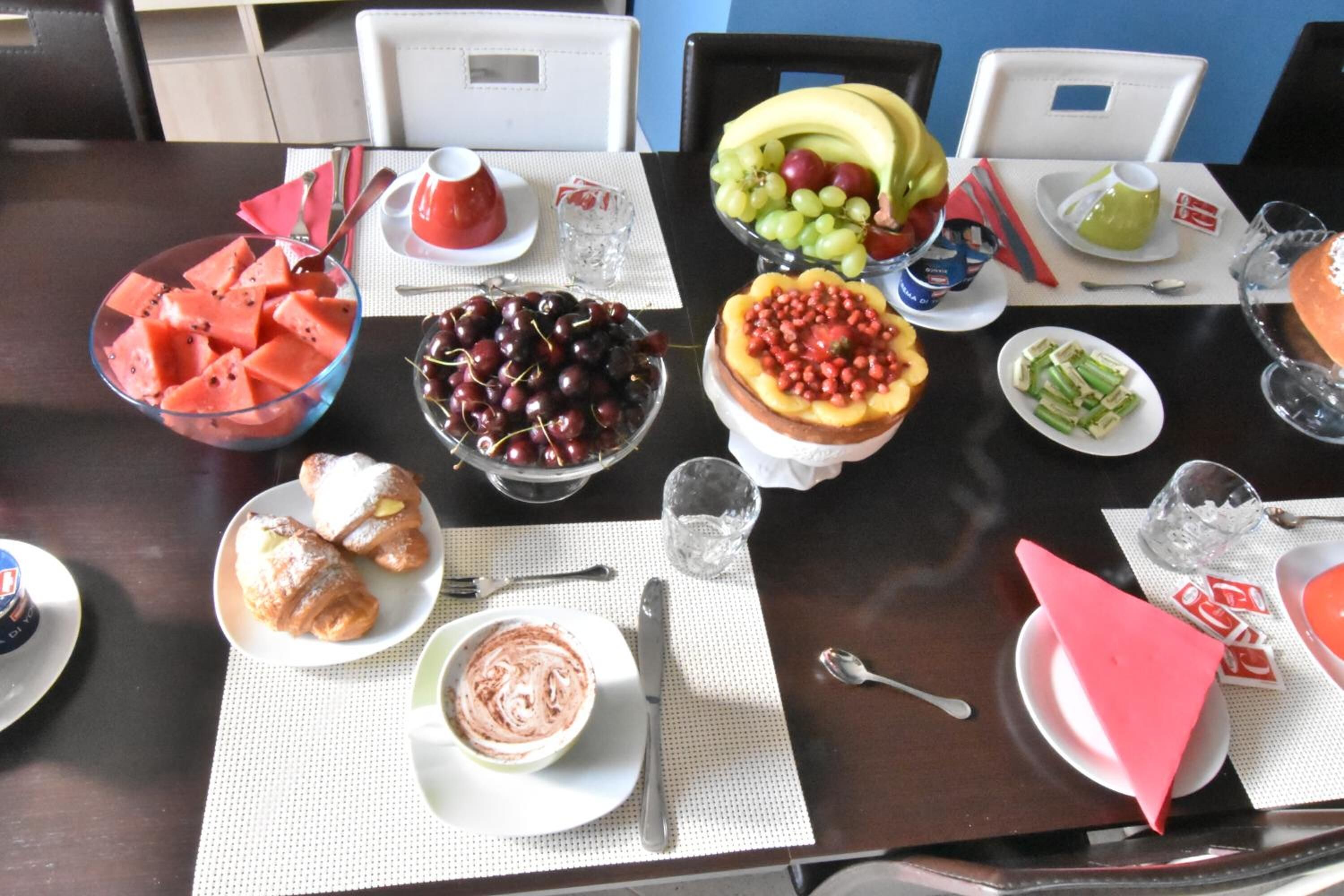A dining table with various food items, including watermelon, cherries, grapes, and a fruit salad.