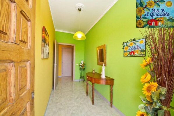 A hallway with a wooden door, a green wall, a table with a white candle, and a wall-mounted sign. - Il Girasole Bed and Breakfast (Palermo)
