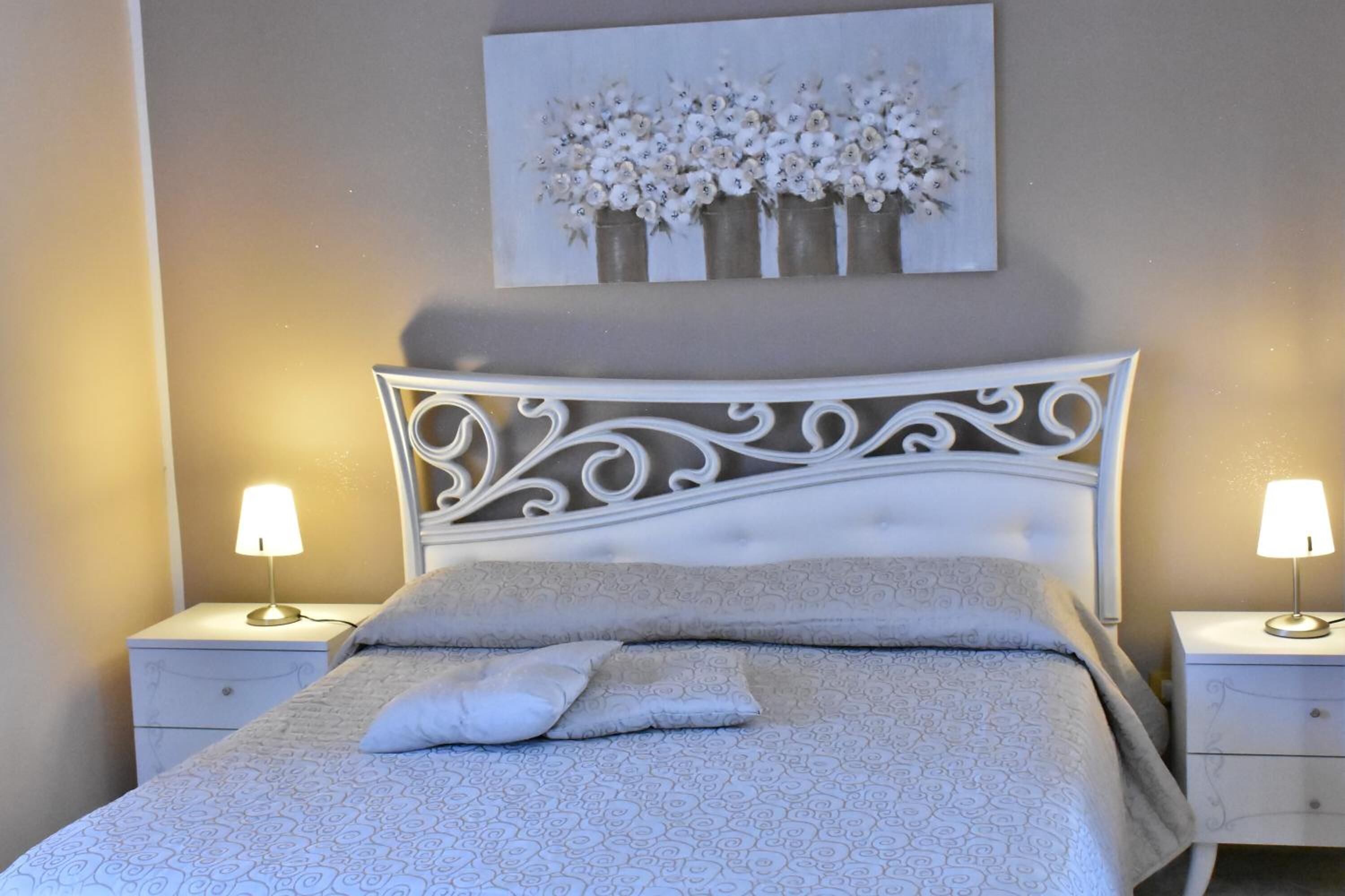 Un lit bien fait, recouvert d’une couvre-lit à motifs et agrémenté d’oreillers, avec deux tables de chevet de chaque côté, chacune surmontée d’une lampe, et une œuvre d’art accrochée au mur au-dessus.