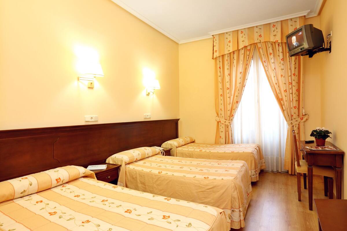 A hotel room with two beds, a desk, a chair, a television, and a window with curtains.