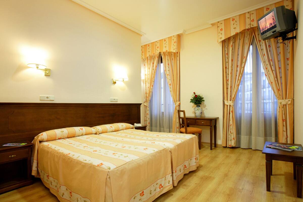 A hotel room with a double bed, a desk, a chair, a television, and curtains.
