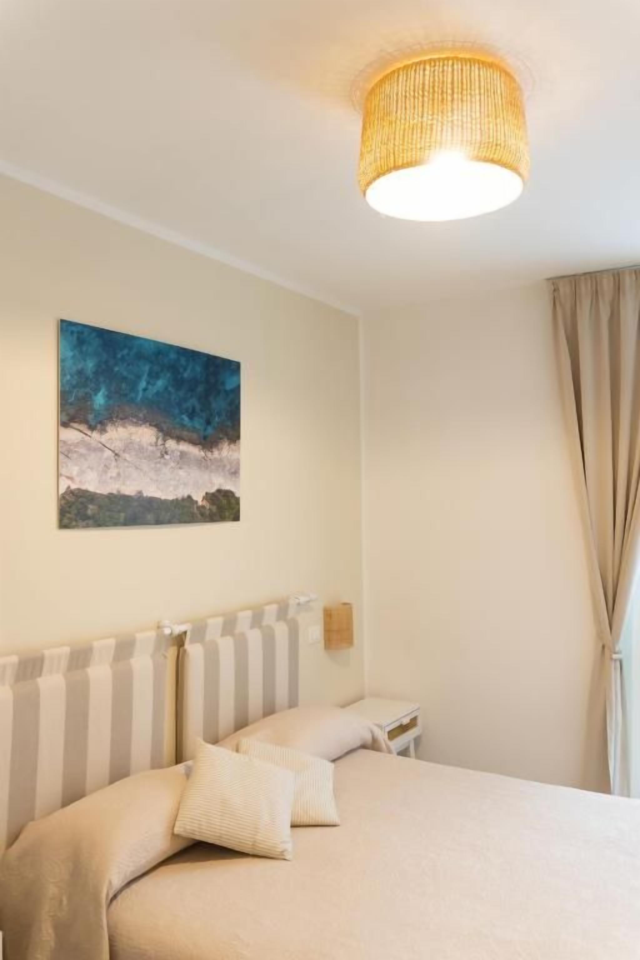 Una habitación de hotel con una cama, un cuadro en la pared, una lámpara y una ventana con cortinas.