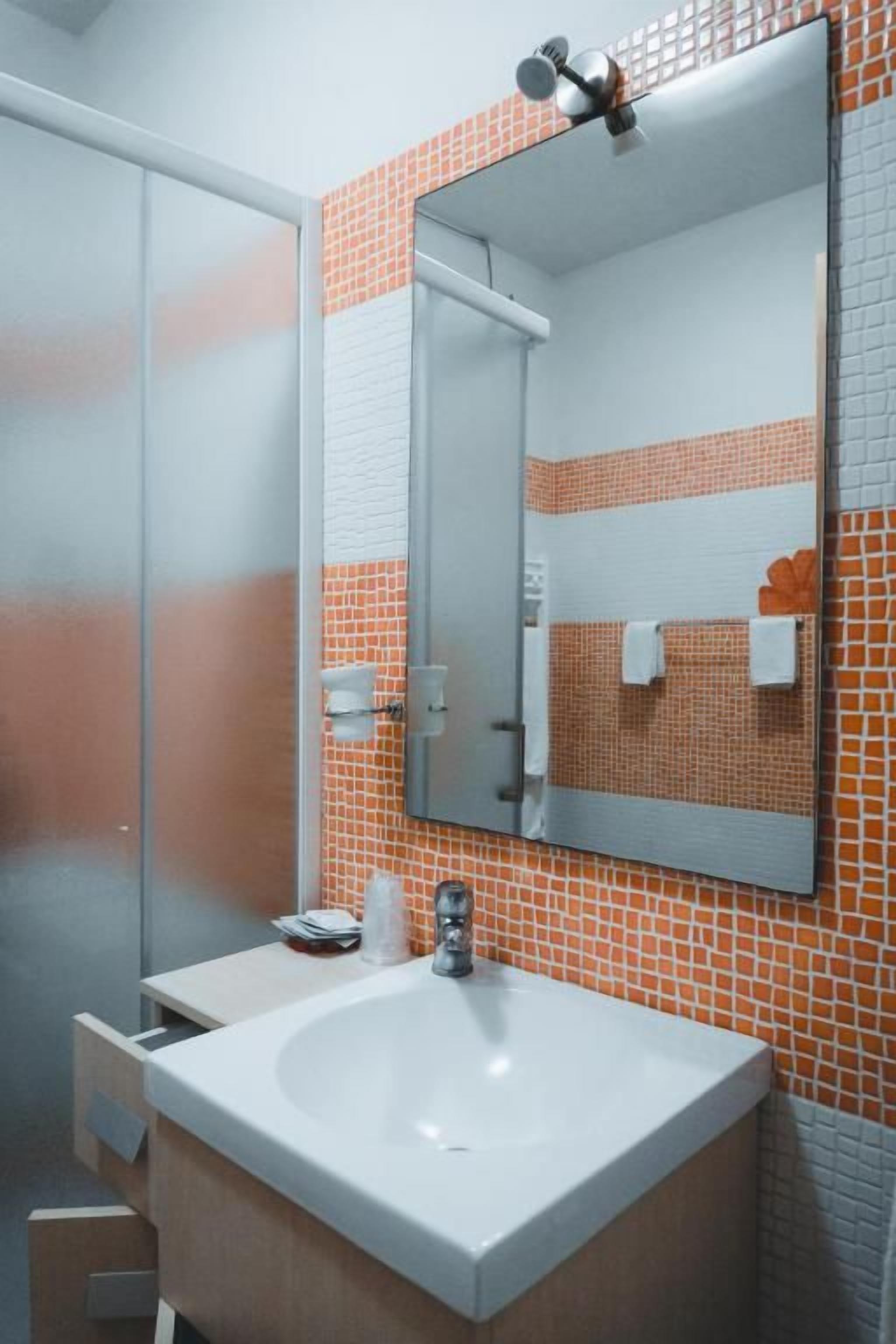 A bathroom with a white sink, a mirror, and orange-tiled walls.