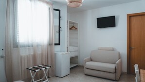 Ein Zimmer mit einem Bett, einem Schreibtisch, einem Stuhl, einem Kleiderschrank, einem Fernseher und einer Tür.